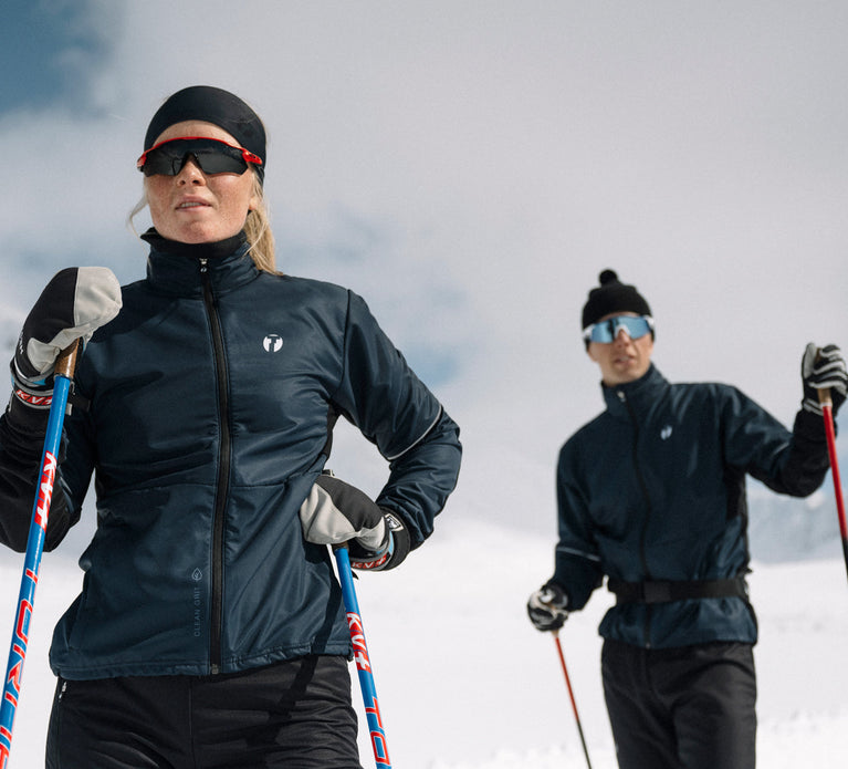 Two people looking over the camera, both wearing Trimtex Ambition skiing jacket and pants