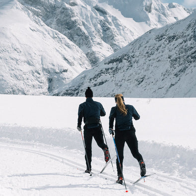 A man and woman skiing past the camera on the mountain in their trimtex Ambition pants and jacket.