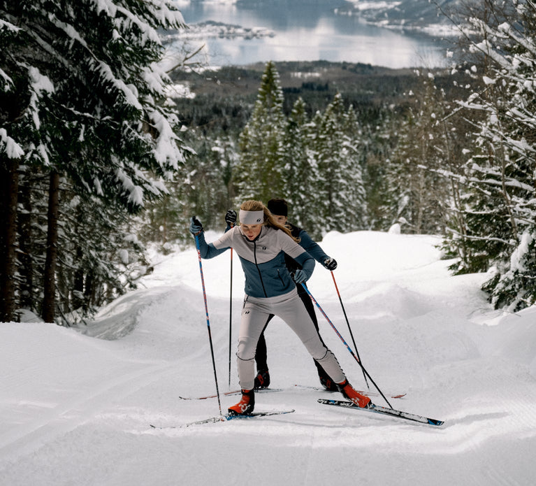 Two people cross country skiing. The woman is wearing Trimtex Ace skiing clothes and a Pulse Merino headband.