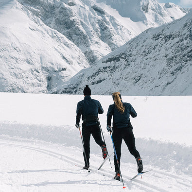 A man and woman skiing past the camera on the mountain in their trimtex Ambition pants and jacket. 