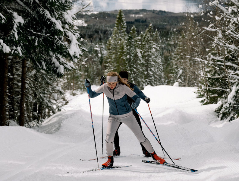 Two people cross country skiing. The woman is wearing Trimtex Ace skiing clothes and a Pulse Merino headband.