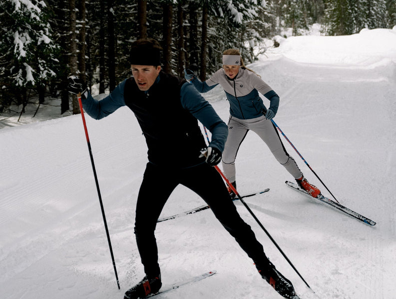 Man and woman are cross-country skiing. They are wearing Ace tracksuits.