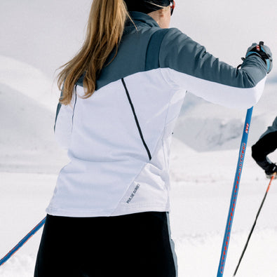 Back of a woman skiing, wearing Trimtex Pulse Jacket. The back has elastic panels and a visible reflective seam across the back.