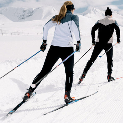 Man and woman skiing away, wearing Trimtex Pulse Ski Jackets, Pants and Vest. 